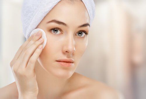 Грижа против бръчките по лицето: Млада жена почиства лицето си с памучен тампон