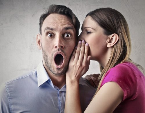 Една жена шепне нещо на ушото на един мъж и клюкарства