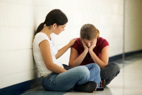 Емоционално нестабилните хора: две момичета са седнали в коридора, на пода, и едното момиче утешава другото.