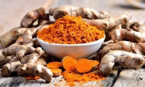 Смляна куркума в бяла порцеланова купичка и корени от куркума