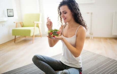 За отслабване на корема: една млада жена седнала на пода, яде салата.