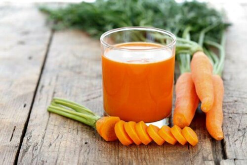 Снимка на сок от моркови в чаша и няколко цели моркова