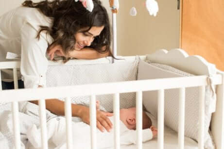Сънят на детето: една млада жена се е надвесила над детско креватче, в което спи бебе