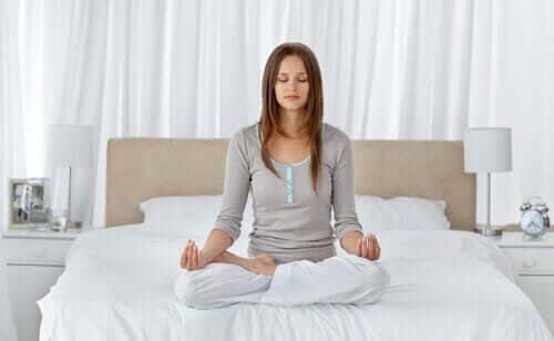 Една млада жена, седнала на легло и медитира.