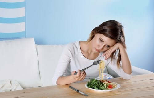 Снимка на млада жена, която изглежда тъжна и се оптва да яде спагети със зеленчуци.