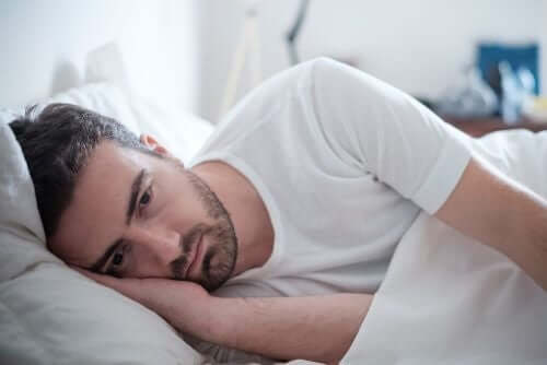 Снимка на един тъжен млад мъж, който лежи в леглото.