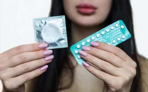 Една млада жена държи противозачатъчни хапчета и кондом