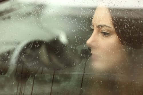 Снимка на лице на тъжна жена, която глед през прозореца, а навън вали дъжд