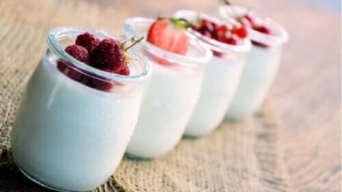 Снимка на четири стъклени бурканчета с кисело мляко и отгоре с различни плодове малини, ягоди и т.н.