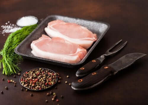 Две сурови парчета сурово свинско филе в чиния и черен пипер в купичка