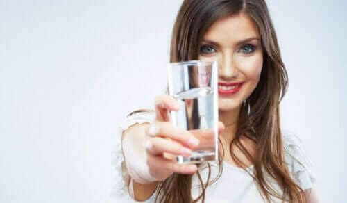 Млада, усмихната жена държи чаша с вода